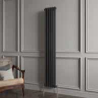 Black vertical radiator against a gray paneled wall with a wooden chair.