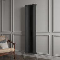 Black vertical radiator against a gray paneled wall with a wooden chair.