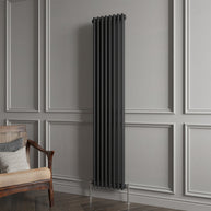 Black vertical radiator against a gray paneled wall with a wooden chair.