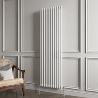 White vertical radiator on a gray paneled wall with a wooden chair and cushions.