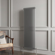 Tall vertical radiator against a gray paneled wall with a wooden chair.