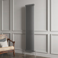 Vertical radiator against a gray paneled wall with a wooden chair.