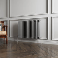 Gray radiator on a wall with wooden flooring and a chair in the corner.