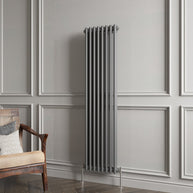 Vertical radiator against a gray paneled wall with a wooden chair.
