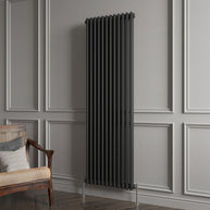 Black vertical radiator against a gray paneled wall with a wooden chair.