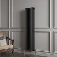 Black radiator against a gray paneled wall with a wooden chair.